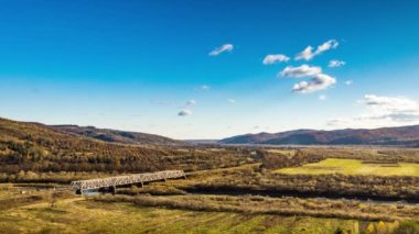 Dağlık arazide renkli ağaçlarla dolu bir nehir üzerindeki demiryolu köprüsü.
