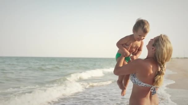 Η μαμά πετάει το γιο της πάνω από τη θάλασσα στις καλοκαιρινές διακοπές κάτω από τον ζεστό ήλιο. — Αρχείο Βίντεο