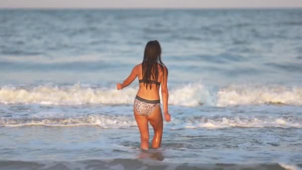 Uma menina com cabelos soltos caminha no mar com ondas e gosta do sol — Vídeo de Stock