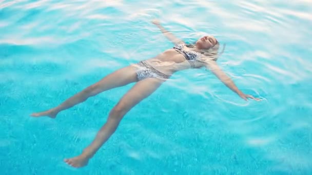 Girl in a in leopard swimsuit swims in a pool with clear water on summer vacation — Stock Video