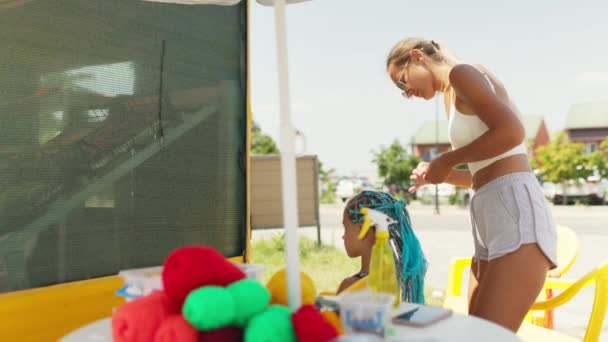 Banyak benang dan pita tergeletak di atas meja dengan latar belakang seorang gadis yang kepang afrika menenun — Stok Video