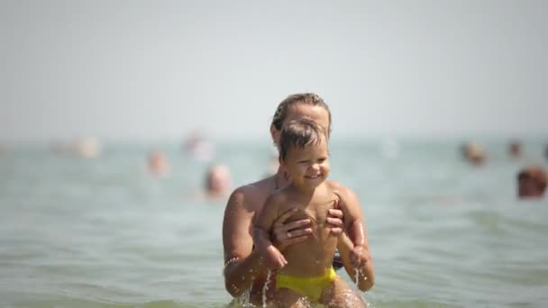 Maman jette son fils au-dessus de la mer en vacances d'été sous le soleil chaud — Video