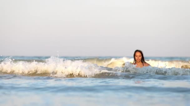 Κορίτσι με βρεγμένα μαλλιά σε λεοπαρδαλέ μαγιό ρίχνει νερό ενώ κάθεται στη θάλασσα — Αρχείο Βίντεο