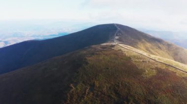 Mavi bulutlu gökyüzünün altındaki dağ sırtında dar yollar
