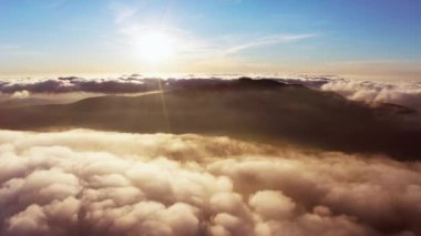 Güneş, gün doğumunda beyaz kabarık bulutların üzerinde parlıyor.