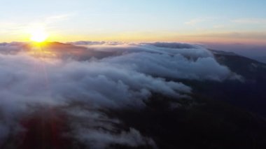 Güneş, gün doğumunda beyaz kabarık bulutların üzerinde parlıyor.