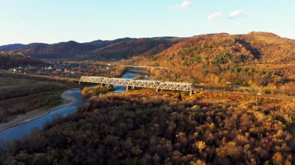 Most kolejowy nad rzeką w górach z kolorowymi drzewami — Wideo stockowe
