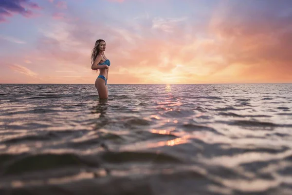 透明感のある水で清らかな河口の暖かい夕日を背景に 優しい青の水着に濡れた髪の細い日焼けした女の子は 彼の周りの美しい自然を楽しんで — ストック写真