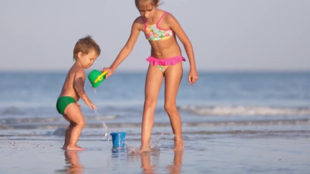Старша сестра грає з молодшим братом біля берега на літніх канікулах — стокове відео