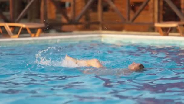 Frau schwimmt in einem Pool mit klarem Wasser vor dem Hintergrund eines sommerlichen Sonnenuntergangs im Urlaub — Stockvideo
