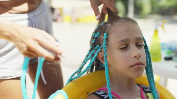 En flicka i kostym väver afrikanska flätor i håret en solig dag — Stockvideo