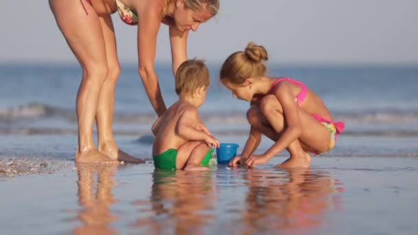 Mom plays with her children: daughter and baby, building beads and castles decorating them with shells — Stock Video