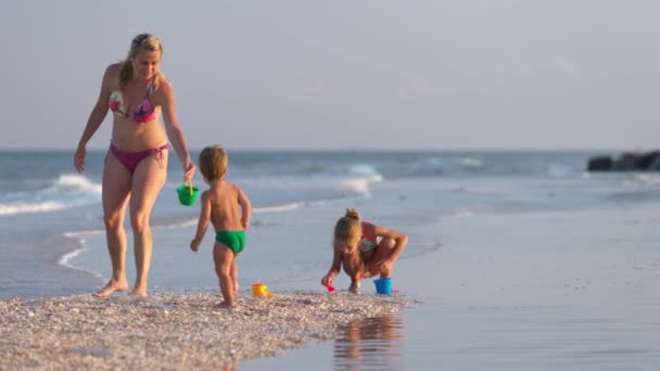 Mamma gioca con i suoi figli: figlia e bambino, costruendo perline e castelli decorandoli con conchiglie — Video Stock