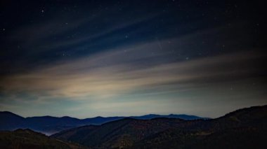 Sonbaharda dağların üzerinde pembe bulutlar olan gece yıldızlı gökyüzü