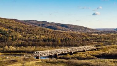 Dağlık arazide renkli ağaçlarla dolu bir nehir üzerindeki demiryolu köprüsü.