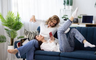 İki kız - telefonu ve dergisi olan kız arkadaşları kanepede oturup şakalara ve sohbetlere gülüyorlar.