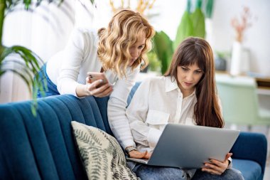 Tişörtlü iki kız telefona ve dairede bir dergiye bakarken bir şey tartışıyorlar.