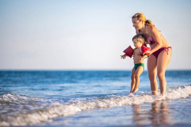 Anne oğlunu yaz tatilinde sıcak güneşin altında denize atıyor.