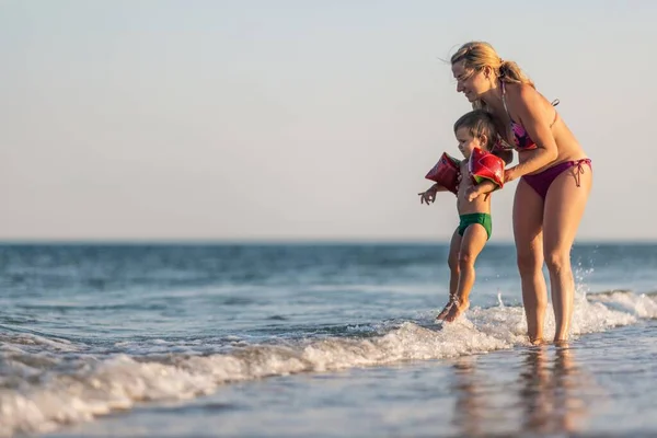 Maman jette son fils au-dessus de la mer en vacances d'été sous le soleil chaud — Photo