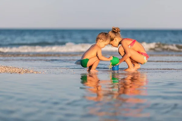Oudere zus spelen met jongere broer aan de grond in de buurt van de kust in de zomer vakantie — Stockfoto
