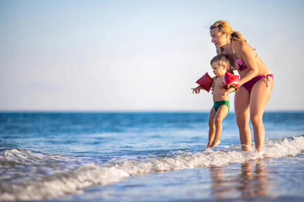 Maman jette son fils au-dessus de la mer en vacances d'été sous le soleil chaud — Photo