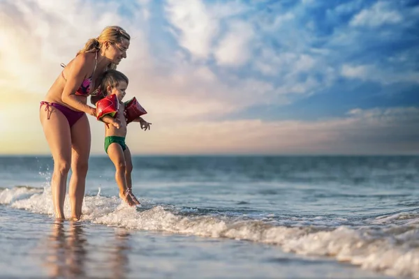 Mamá arroja a su hijo sobre el mar en vacaciones de verano bajo el cálido sol — Foto de Stock