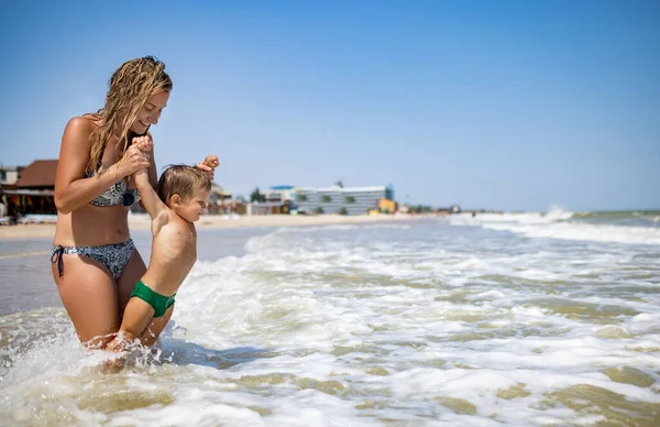 Maman jette son fils au-dessus de la mer en vacances d'été sous le soleil chaud — Photo