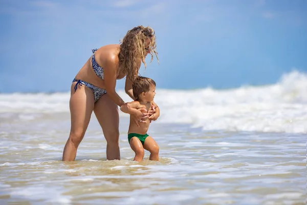 Mamá arroja a su hijo sobre el mar en vacaciones de verano bajo el cálido sol — Foto de Stock