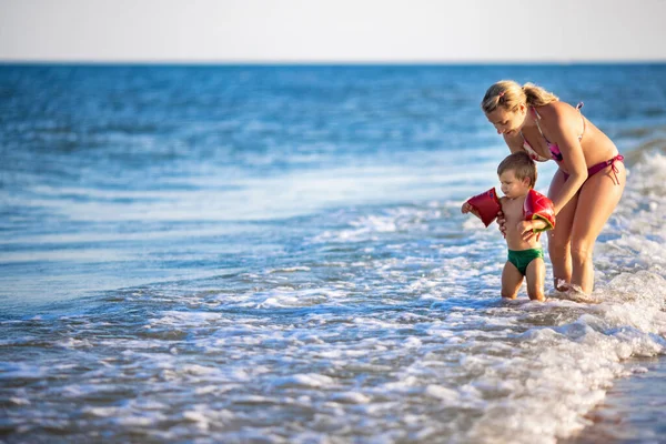 Mamá arroja a su hijo sobre el mar en vacaciones de verano bajo el cálido sol — Foto de Stock