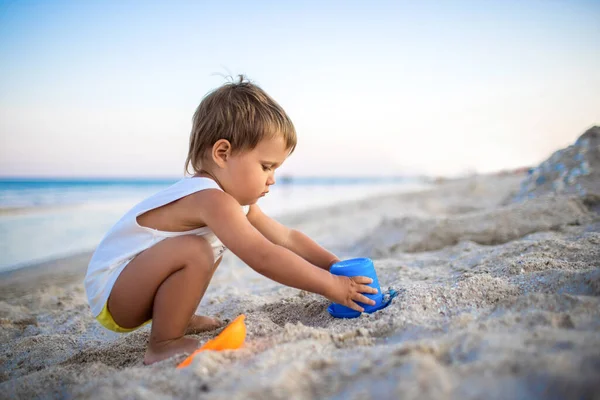 Chico jugando con juguetes en la playa construyendo perlas y torretas sonriendo a alguien detrás de las escenas en las vacaciones de verano —  Fotos de Stock