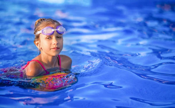 En flicka i en ljus baddräkt simmar med en uppblåsbar boll i en pool med klart vatten en sommarkväll — Stockfoto