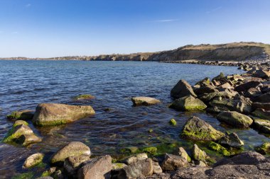 Sakin Bulgar deniz manzarası, sakin mavi yansıtıcı Karadeniz ve parlak güneşli akşam günbatımına karşı eski kayalık taşlar.