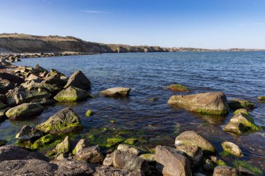 Sakin Bulgar deniz manzarası, sakin mavi yansıtıcı Karadeniz ve parlak güneşli akşam günbatımına karşı eski kayalık taşlar.