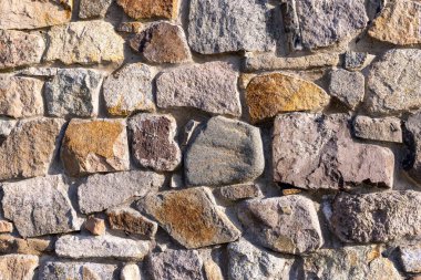 Parlak akşam güneşi altında eski, eski, düz olmayan, tarihi taşlarla kaplı antik bir duvardan kalma gri bir arka plan.