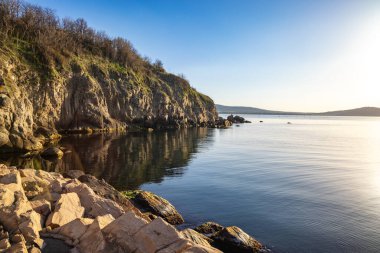 Sakin Bulgar deniz manzarası, sakin mavi yansıtıcı Karadeniz ve parlak güneşli akşam günbatımına karşı eski kayalık taşlar.