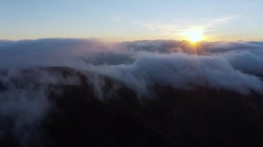 Güneş, gün doğumunda beyaz kabarık bulutların üzerinde parlıyor.