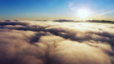 Güneş, gün doğumunda beyaz kabarık bulutların üzerinde parlıyor.