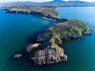Vahşi bir taş ve kumlu sahil manzarası. Karanlık, nemli deniz kumları ve yansıtıcı yay yakınlarındaki kayalık kayalıklar. Karadeniz, Bulgaristan 'ın parlak, güneşli günbatımı ışığı altında.