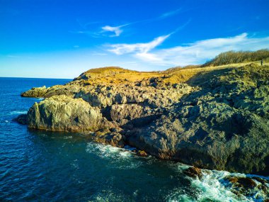 Vahşi bir taş ve kumlu sahil manzarası. Karanlık, nemli deniz kumları ve yansıtıcı yay yakınlarındaki kayalık kayalıklar. Karadeniz, Bulgaristan 'ın parlak, güneşli günbatımı ışığı altında.
