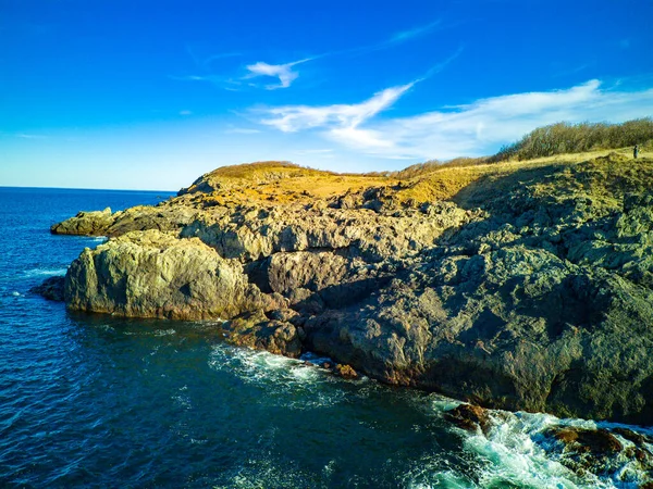 Vahşi bir taş ve kumlu sahil manzarası. Karanlık, nemli deniz kumları ve yansıtıcı yay yakınlarındaki kayalık kayalıklar. Karadeniz, Bulgaristan 'ın parlak, güneşli günbatımı ışığı altında.