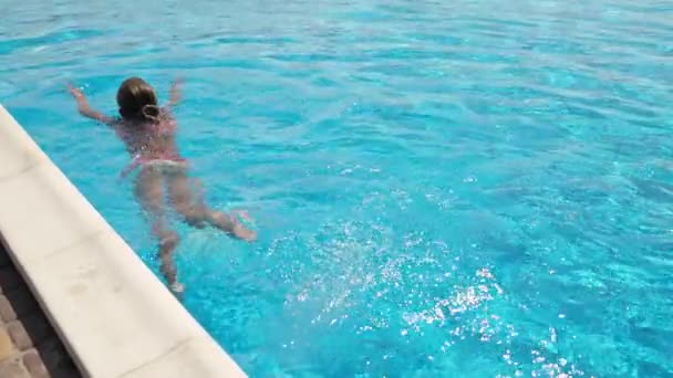 Дівчина в рожевому купальнику в фіолетових окулярах плаває на басейні з блакитною водою в літній день — стокове відео