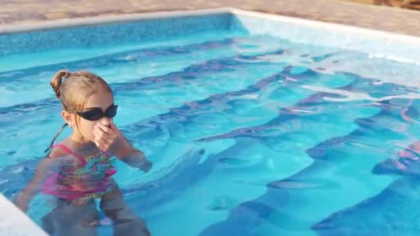 Una chica en un traje de baño brillante con gafas de baño se sumerge en una piscina con agua transparente clara — Vídeo de stock