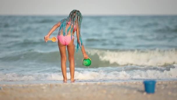 夏の衣装を着たアフリカ人の花嫁の女の子は、晴れた日の下で波と海の近くのシェルでビーチで再生されます — ストック動画