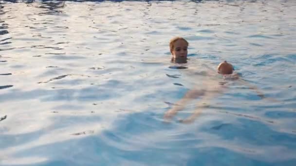 Starší sestra pomáhá své malé sestřičce v růžových plavkách naučit se plavat v bazénu čisté vody — Stock video
