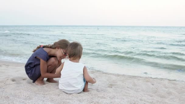 Chica ayudando a su hermano pequeño a buscar conchas marinas en la arena de la costa — Vídeos de Stock