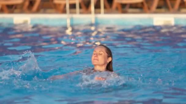 Kadın tatilde yaz günbatımının arka planında temiz suyla havuzda yüzer. — Stok video