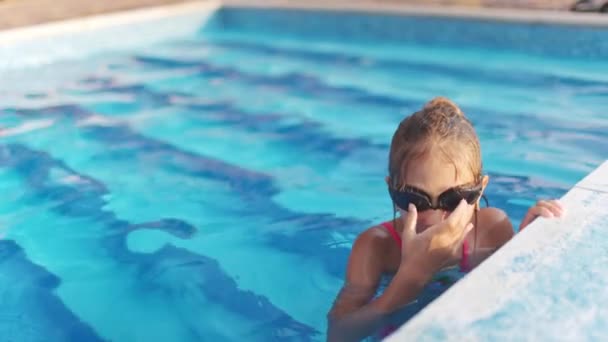 Uma menina em um maiô brilhante com óculos de natação mergulha em uma piscina com água transparente clara — Vídeo de Stock