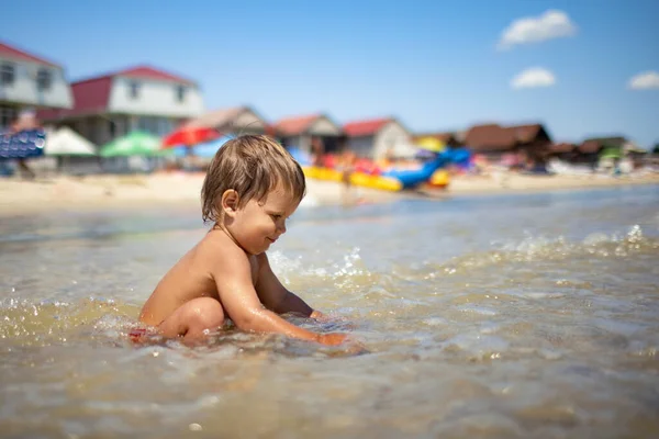 Niño recoge conchas y guijarros en el mar en un fondo arenoso bajo el sol de verano en unas vacaciones —  Fotos de Stock