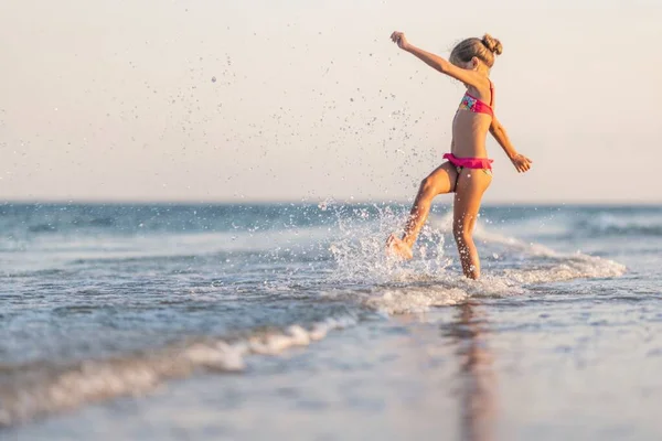 Ragazza che gioca con le onde calci e filatura sotto il sole estivo godendo la vacanza — Foto Stock