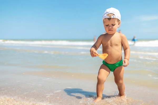 Ragazzo raccoglie conchiglie e ciottoli in mare su un fondo sabbioso sotto il sole estivo in vacanza — Foto Stock